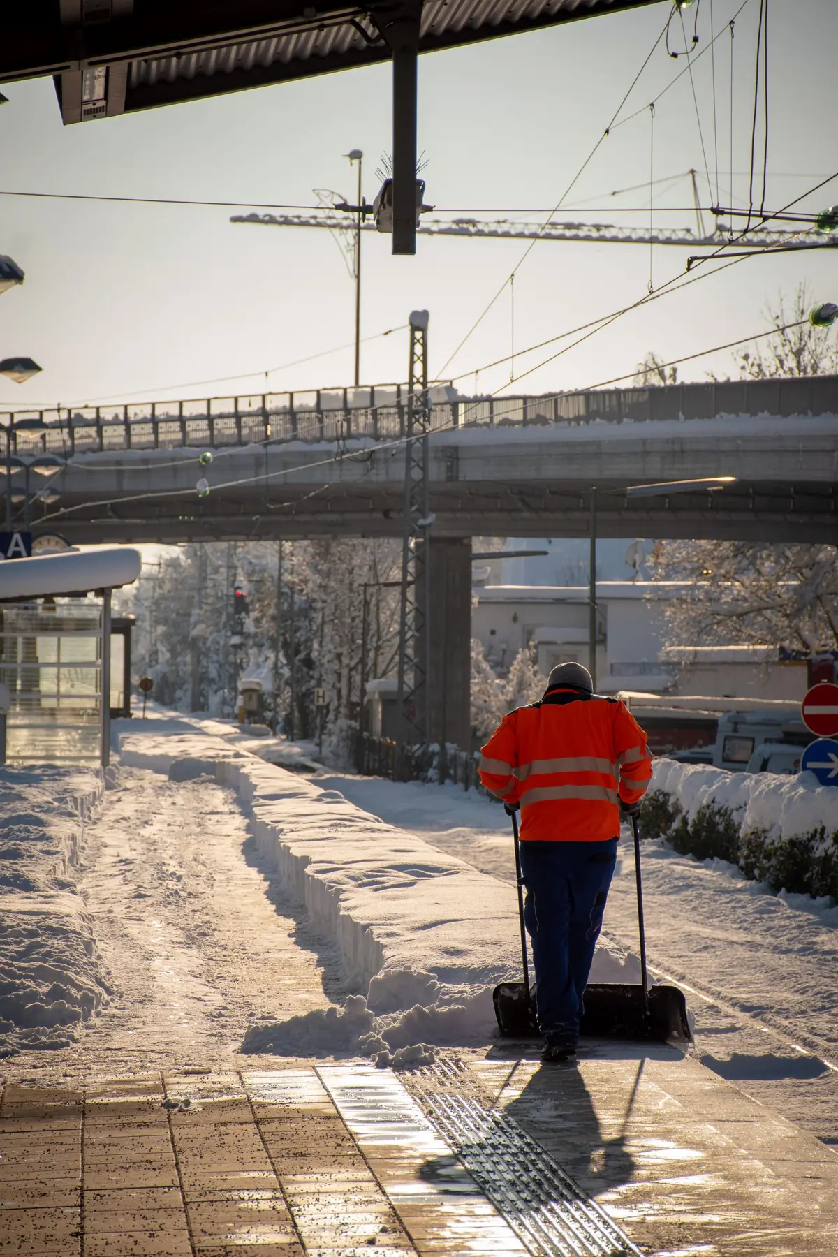 Winterdienst: Mitarbeiter in Warnweste räumt Schnee vom Gehweg